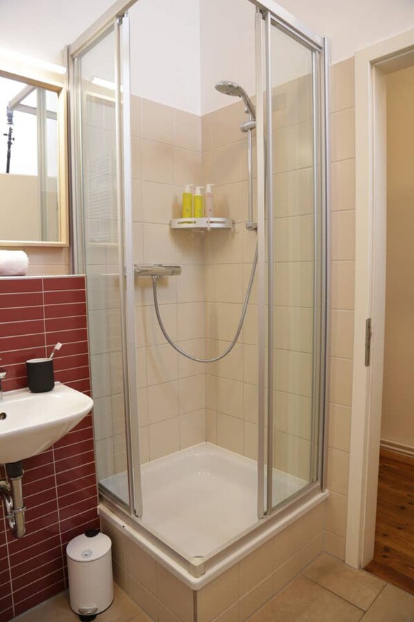 A glass-enclosed shower with a white sink and red-tiled walls. - Bright and modern 2-room apartment in Prenzlauer Berg (3) (Berlin)
