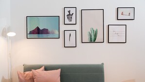 Una habitación con un sofá verde, una lámpara de pie y cuatro cuadros enmarcados en la pared.