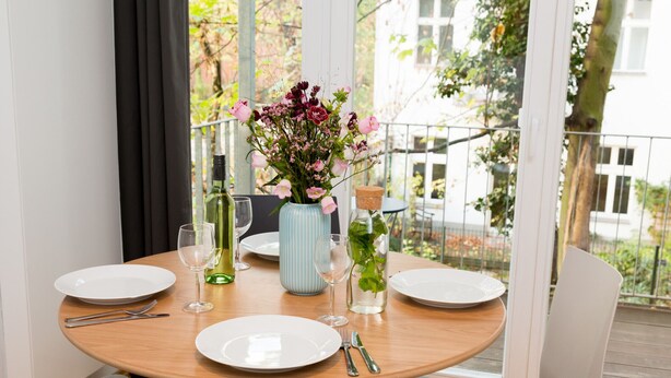 Una mesa redonda de comedor con platos blancos, cubiertos y un florero.