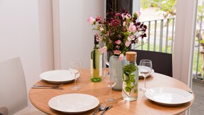 Una mesa de madera redonda dispuesta para comer, con platos blancos, cubiertos y un jarrón con flores.