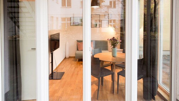 Un interior moderno con piso de madera, una mesa redonda con sillas, un sofá y un televisor sobre un mueble.