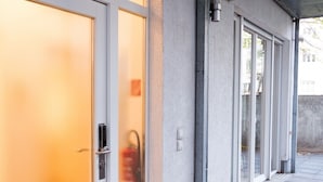 Una entrada de edificio con un toldo, una puerta con cerradura electrónica y una lámpara fijada a la pared.