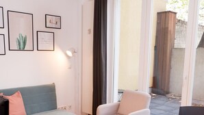 Una sala de estar moderna con sofá, sillón y una mesa redonda. Hay cuadros en la pared y un ventanal con cortinas.