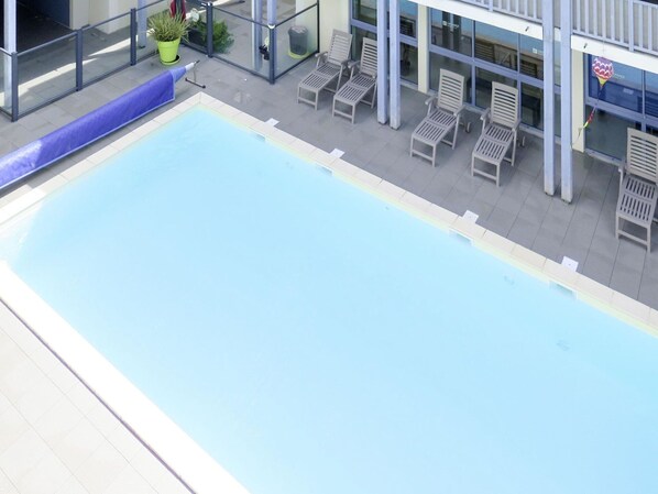 A rooftop pool with a clear blue water surface, surrounded by lounge chairs and potted plants.