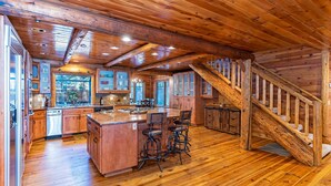 Una cocina amplia con armarios de madera, una isla central con taburetes altos y una escalera de madera.