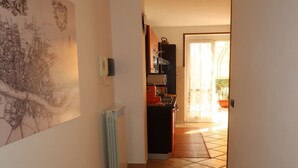 A narrow hallway with a radiator, a wall-mounted telephone, and a door leading to a kitchen area with a stove and cabinets. - Nice apartment for 4 people with WIFI, A/C, TV and terrace (Civezza)