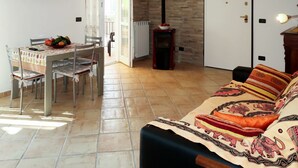 A living room with a sofa, a dining table with chairs, a TV mounted on the wall, and a fireplace. - Nice apartment for 4 people with WIFI, A/C, TV and terrace (Civezza)