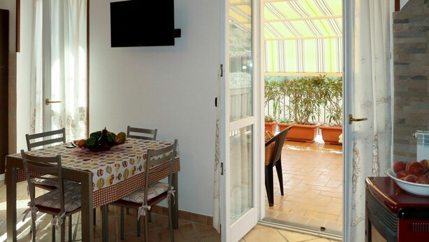 A dining area with a table set for four, chairs, a television mounted on the wall, and a view of an outdoor patio with potted plants. - Nice apartment for 4 people with WIFI, A/C, TV and terrace (Civezza)