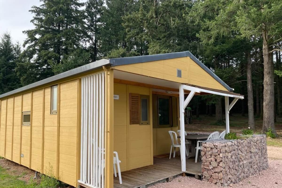 Een gele blokhut met een overdekte veranda, een stenen muur en een klein zitgedeelte buiten.