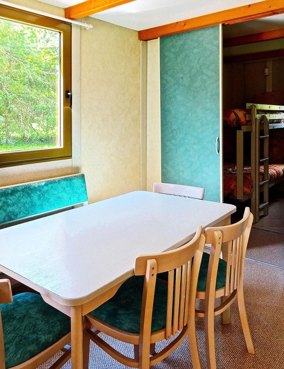 A room with a white table, green cushioned benches, and a window with a view of greenery.