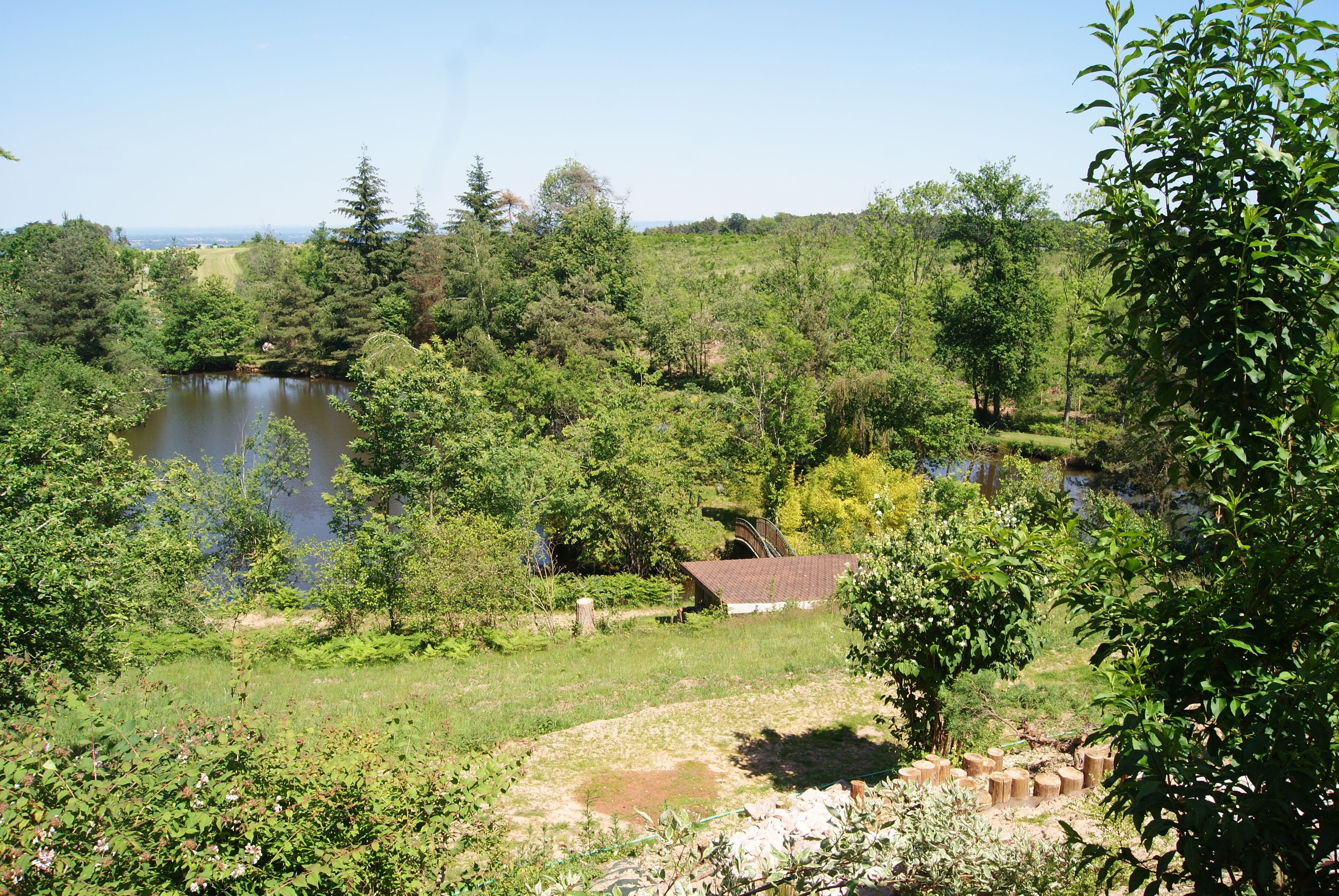 A natural landscape with a lake, dense greenery, and a small building with a sloped roof.