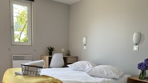 Une chambre d’hôtel avec deux lits, un bureau, une chaise, une fenêtre et un luminaire fixé au mur.