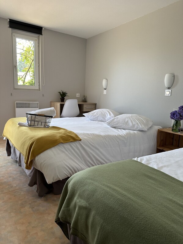 Een hotelkamer met twee bedden, een bureau, een stoel, een raam en een wandlamp.