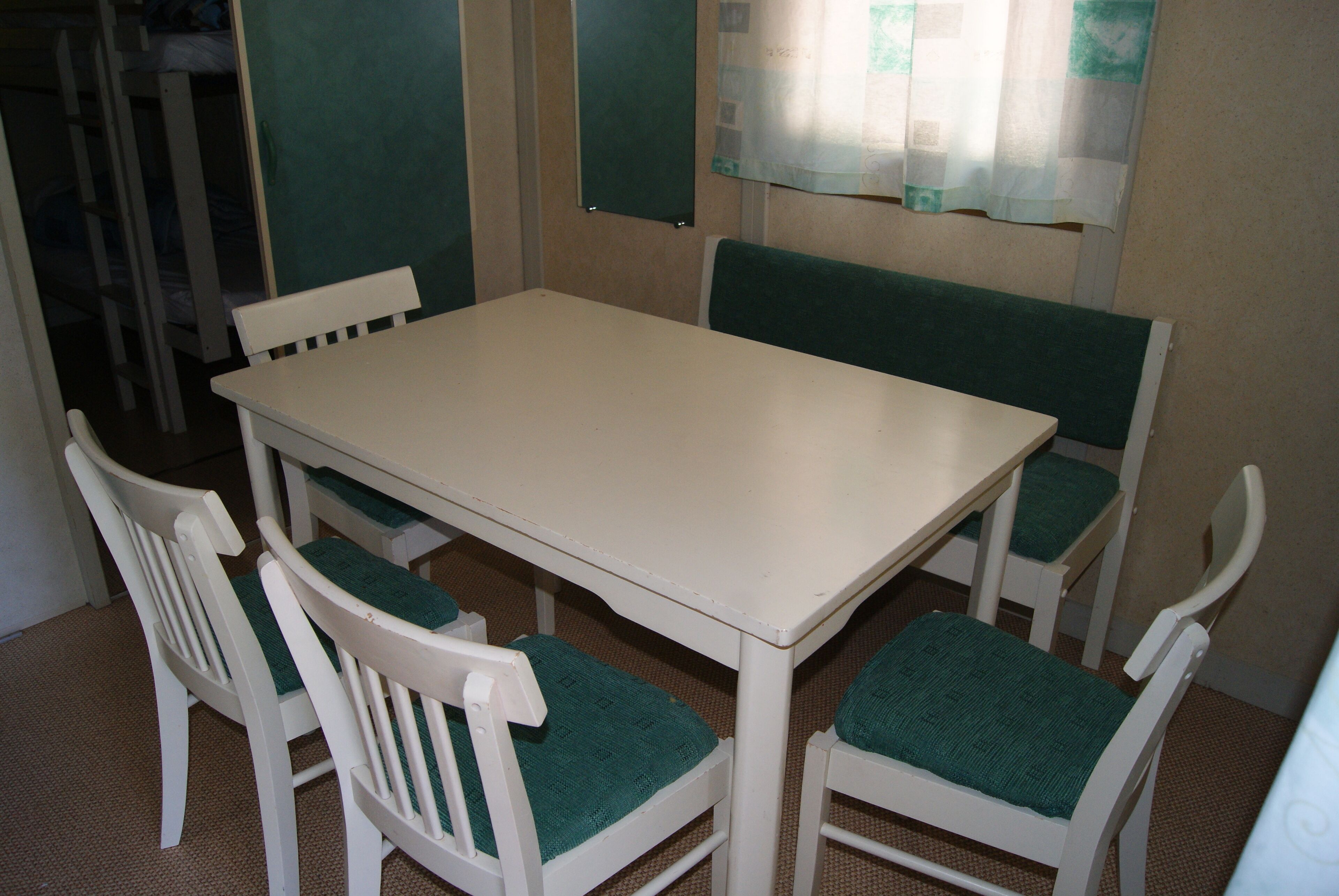 Un petit coin repas avec une table blanche et quatre chaises blanches dotées de coussins verts.
