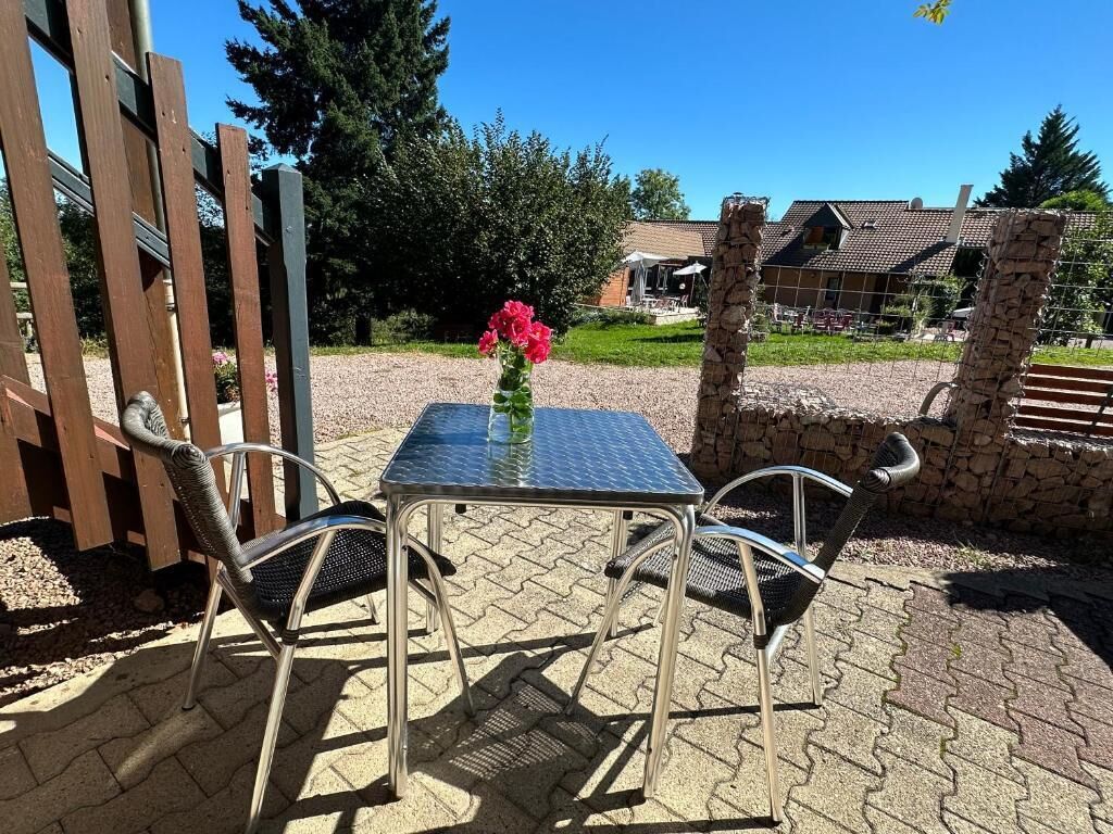 Une terrasse extérieure avec une table et des chaises en métal, un vase rempli de fleurs et un mur en pierre.