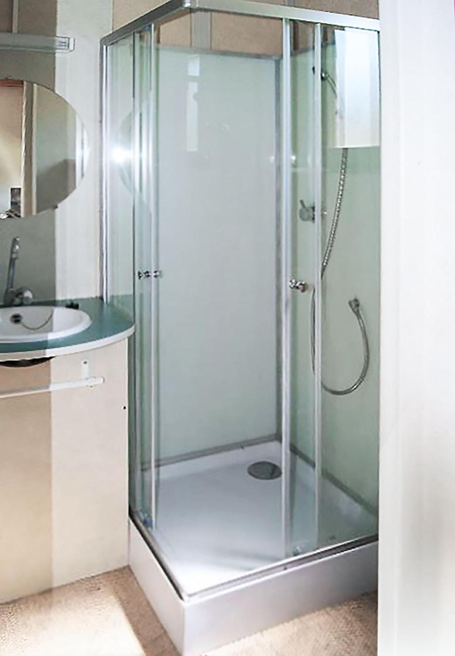 Une douche en verre, avec un lavabo et un miroir, dans une salle de bain.