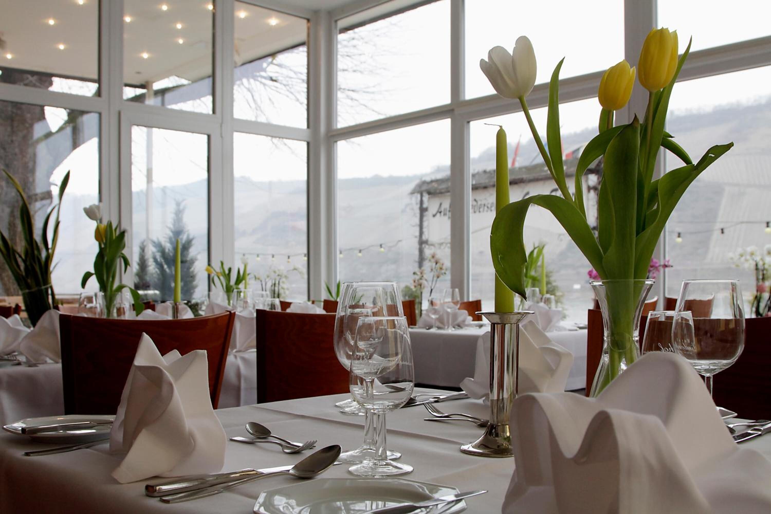 Ein Esstisch ist mit weißen Tischdecken, klarem Glas und Tulpen in Vasen gedeckt.