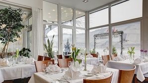Um restaurante com mesas postas para refeições, grandes janelas e vista para as montanhas.