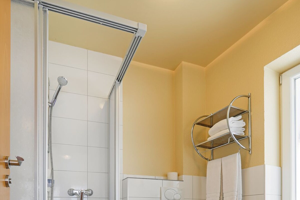 A bathroom with a glass-enclosed shower, a toilet, and a towel rack with towels.