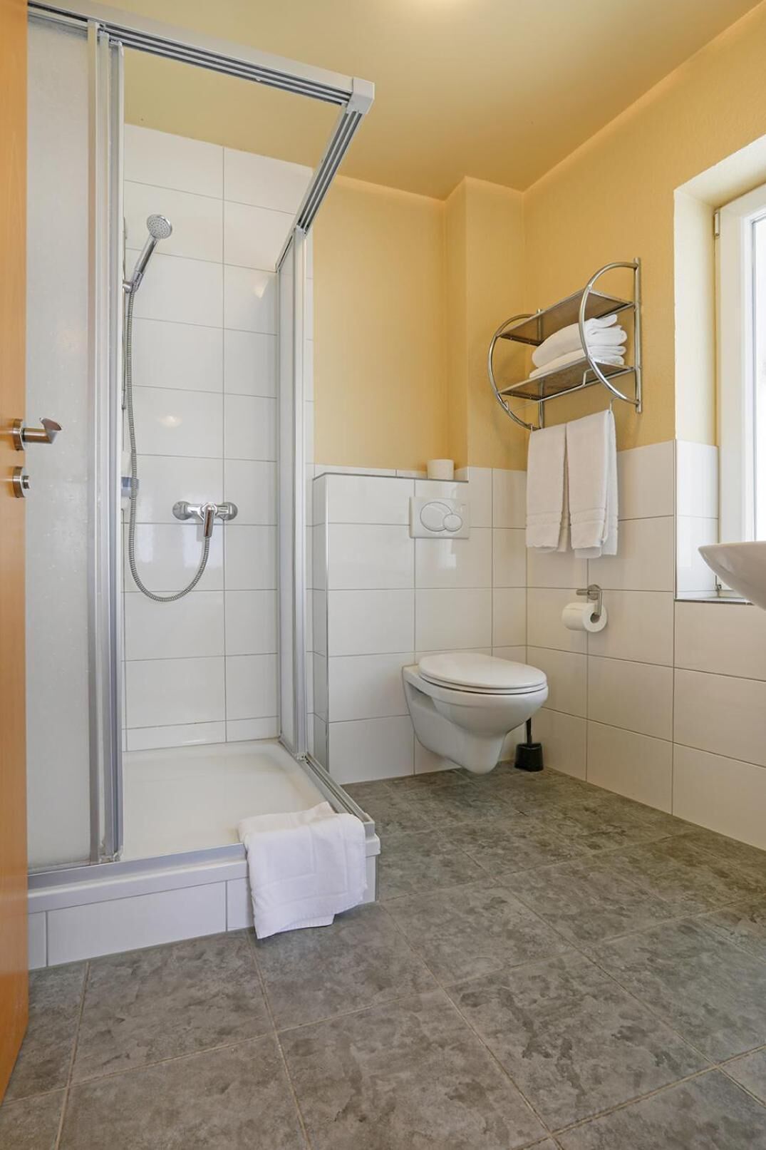 Ein Badezimmer mit einer gläsernen Duschkabine, einer Toilette und einem Handtuchhalter mit Handtüchern.