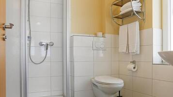 Ein Badezimmer mit einer gläsernen Duschkabine, einer Toilette und einem Handtuchhalter mit Handtüchern.