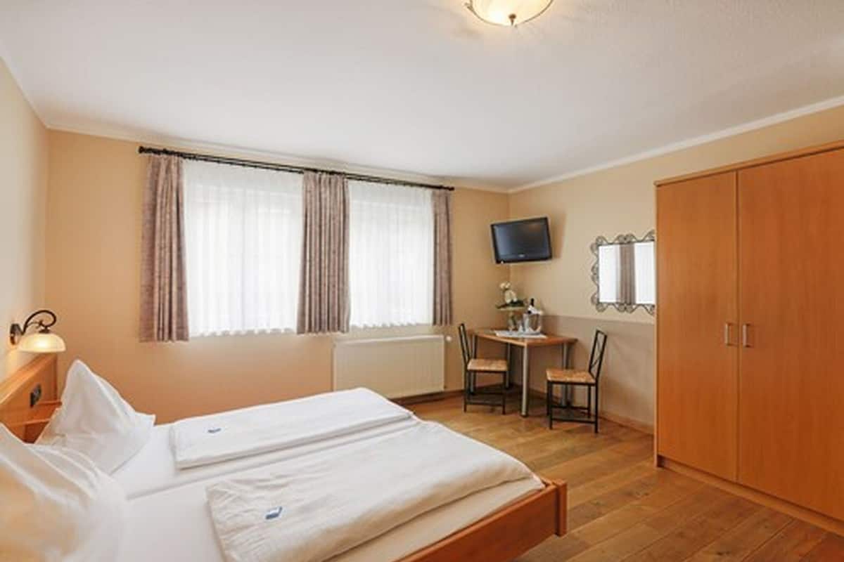 A hotel room with a bed, a desk, a chair, a television, and a wardrobe.