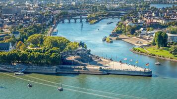 Eine Vogelperspektive einer Stadt an einem Fluss, mit einer markanten Festung, einer Brücke und einer Seilbahn.