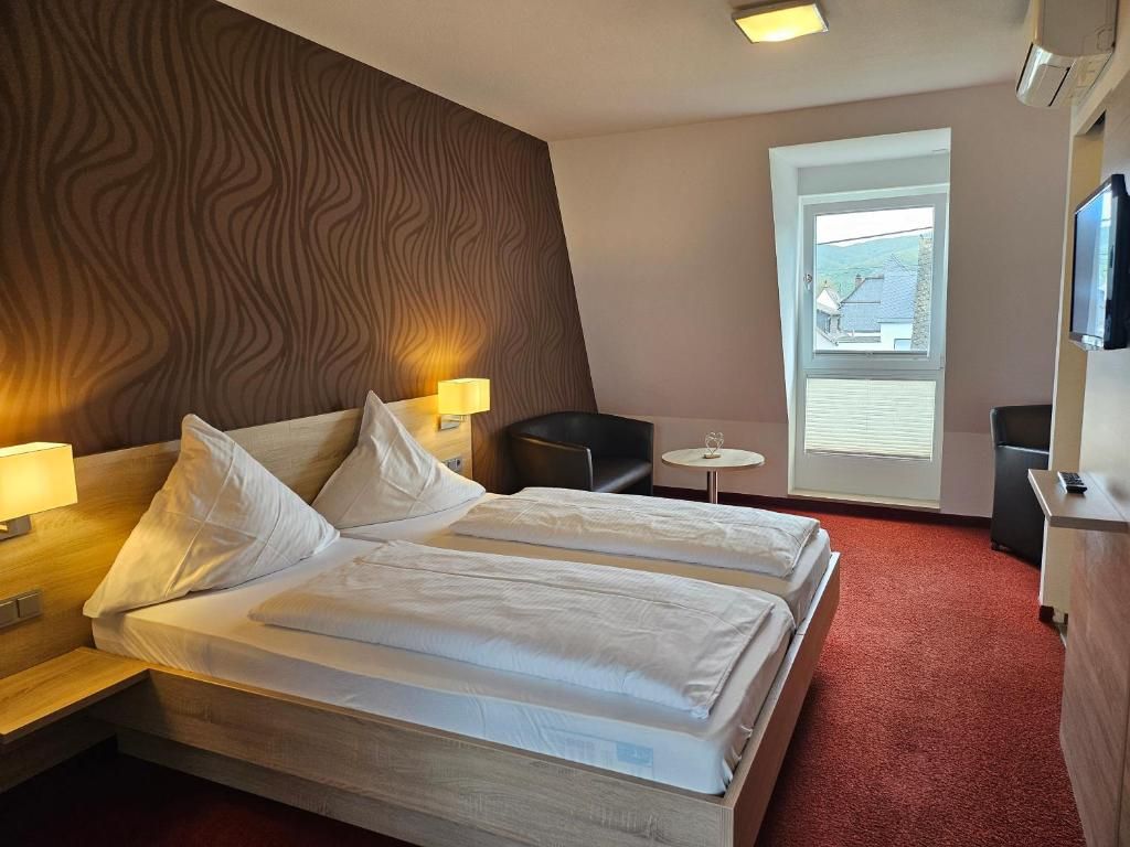 Ein Hotelzimmer mit zwei Betten, einem kleinen Tisch, einem Sessel, einem Fernseher und einem Fenster mit Jalousien.