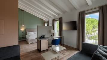 Een moderne hotelkamer met een bed, bureau, stoel, televisie en balkon met uitzicht op bomen.