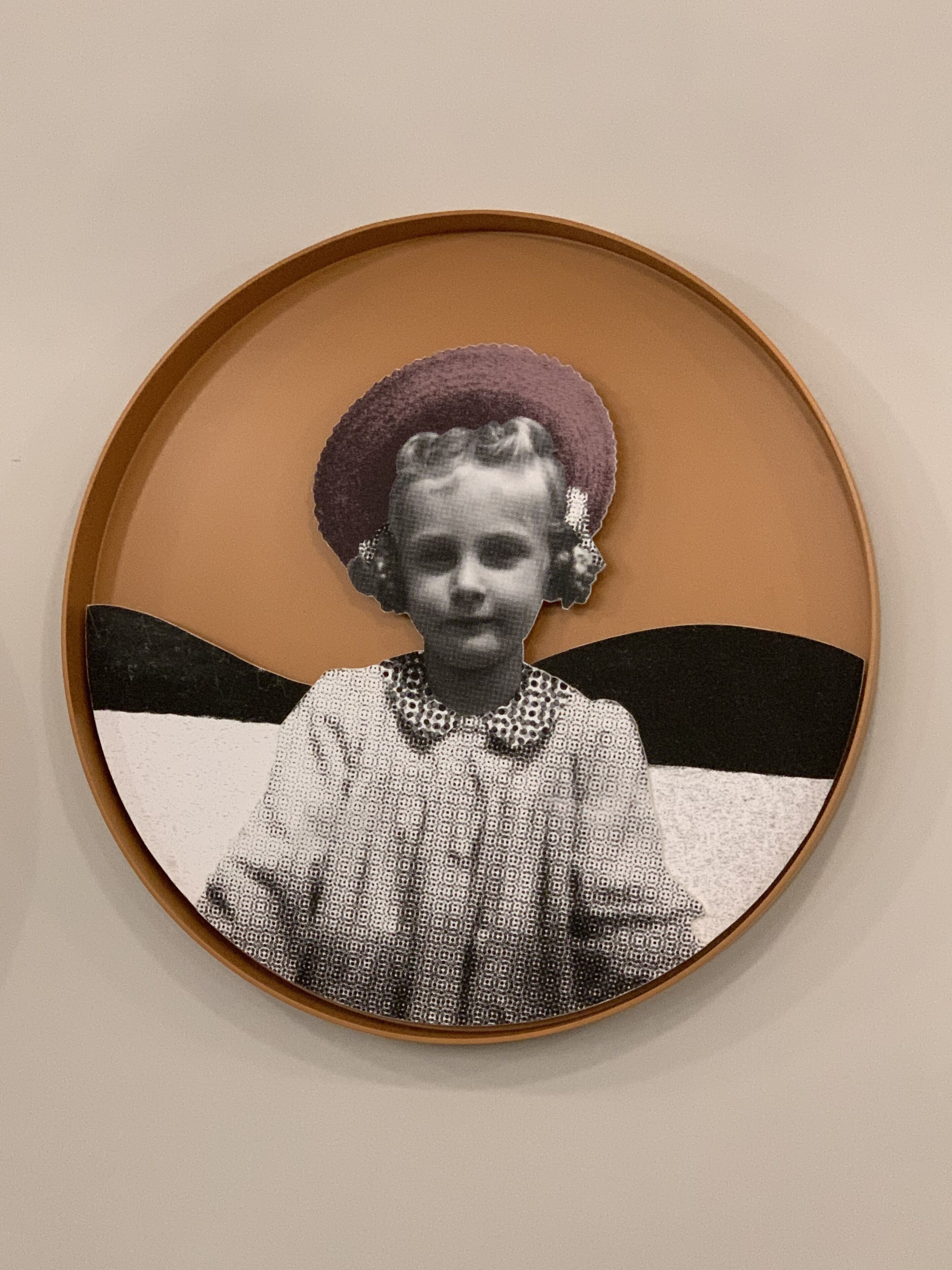 A circular framed photograph with a vintage appearance, featuring a person in a patterned dress and a hat.