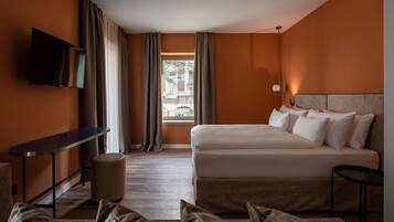 Una camera d'albergo con un letto, una TV a muro, una scrivania e una finestra con tende.