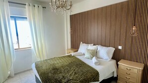 A bedroom with a large bed, a chandelier, a wooden slat wall, and a nightstand.