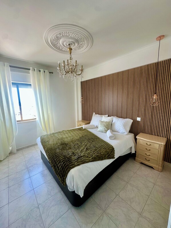 A bedroom with a large bed, a chandelier, a wooden slat wall, and a nightstand.