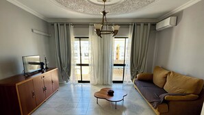 A living room with a sofa, a coffee table, a TV on a wooden cabinet, and a ceiling with decorative molding.