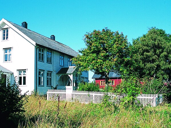 A two-story house with a white exterior and a grey roof, surrounded by a white picket fence and lush greenery. - 15 Person Holiday Home in Flatanger (Flatanger)