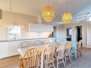 A modern kitchen with white cabinets, a wooden dining table, and wicker pendant lights. - Holiday Home Near Scenic Limfjord (Logstor)