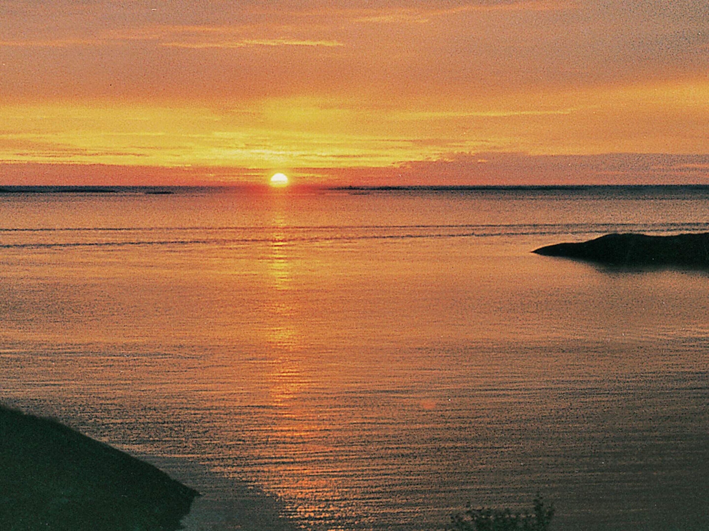 A sunset over a calm sea with a silhouette of land in the distance.