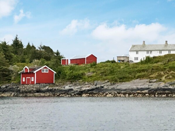 A coastal landscape with a red building, a white building, and a rocky shoreline. - 11 Person Holiday Home in Bud (Hustadvika)