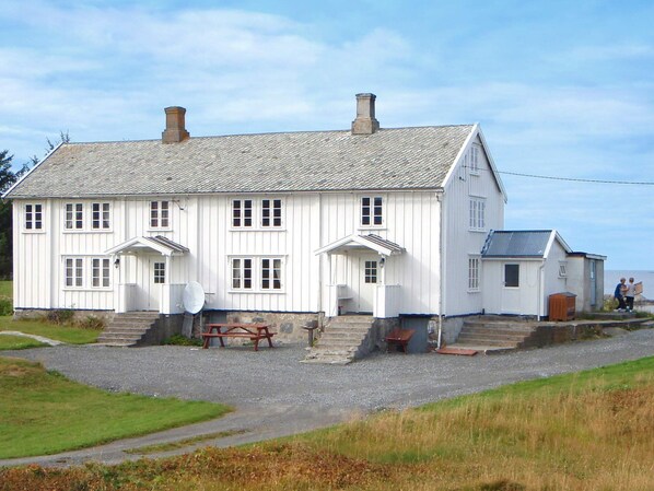 Une maison blanche à deux étages, avec une allée en gravier et une table de pique-nique.