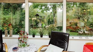 A room with a large window overlooking a garden, a round table with a lace tablecloth, and a black leather chair. - 6 Person Holiday Home in Roslev-by Traum (Roslev)