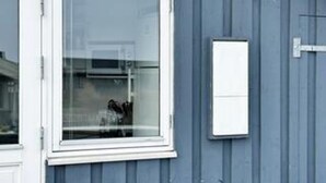 Una ventana con marco blanco, un pequeño cuadro eléctrico blanco en la pared y una pared exterior azul.