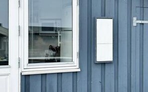 A window with a white frame, a small white electrical box on the wall, and a blue exterior wall.