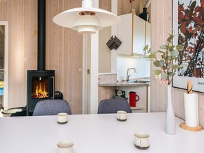 A cozy room with a fireplace, a dining table with chairs, and a kitchen area. - 4 Star Holiday Home in Borkop (Borkop)