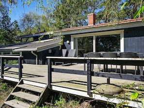 Une terrasse en bois avec des sièges extérieurs et une vue sur un bâtiment doté de grandes fenêtres.