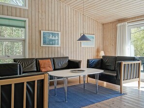 A modern living room with a wooden paneled wall, a black leather sofa, a white coffee table, and a blue rug. - 14 Person Holiday Home in Nexo (Nexø)