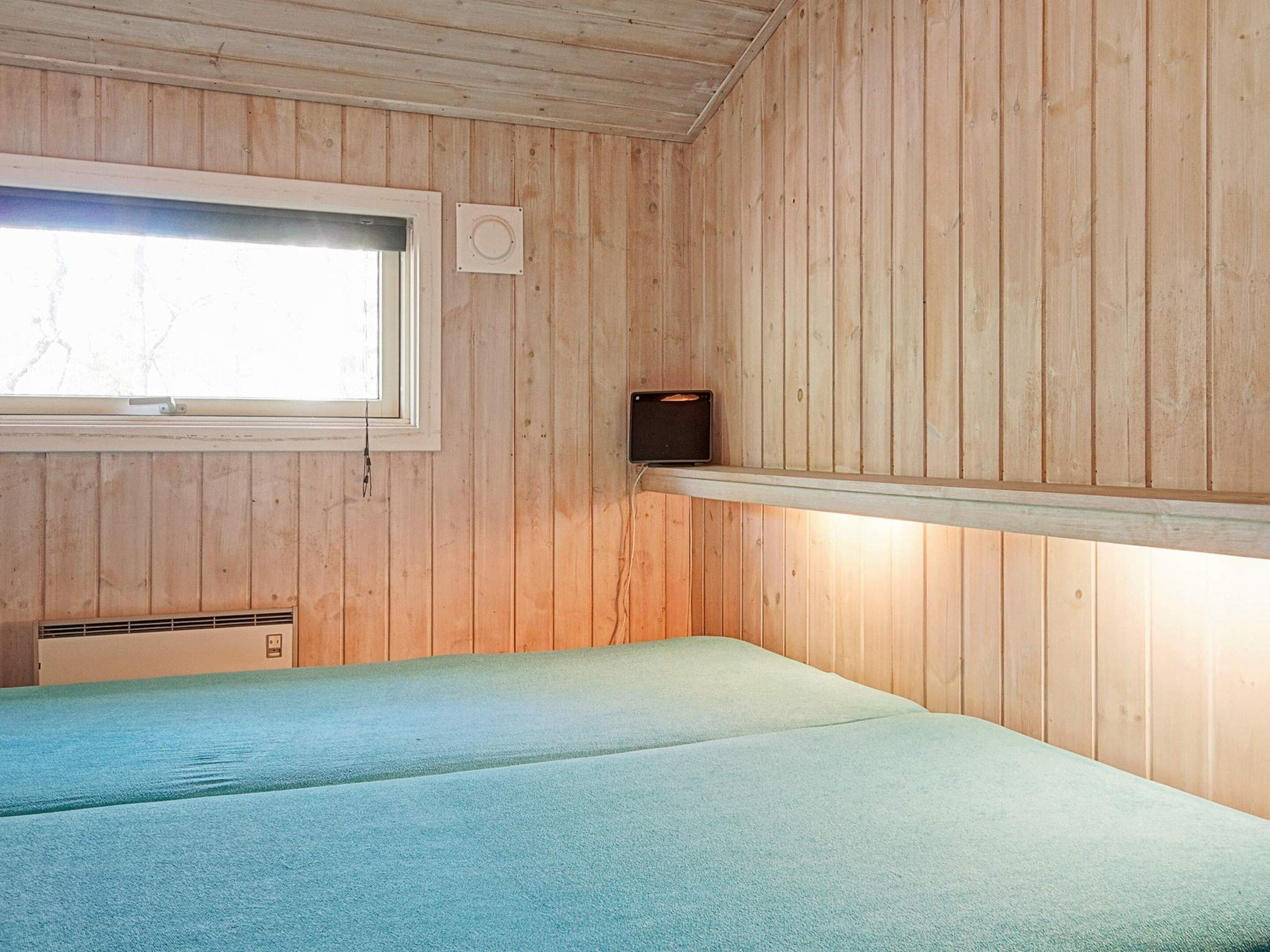 A room with wooden walls, a window, a bed, and a shelf with a speaker.