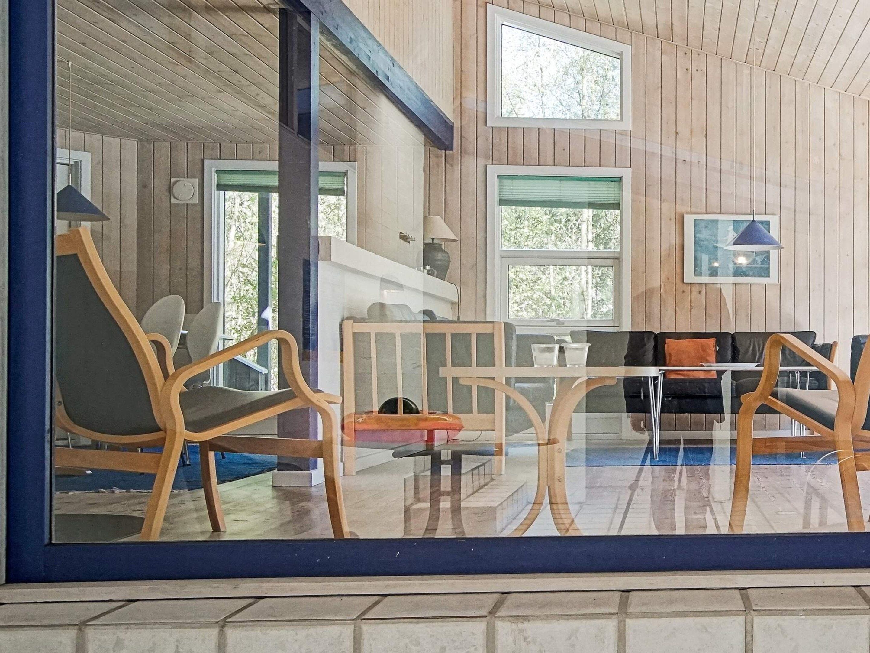 Una habitación con paredes de madera, un separador de vidrio y una zona de estar con sillas y una mesa.