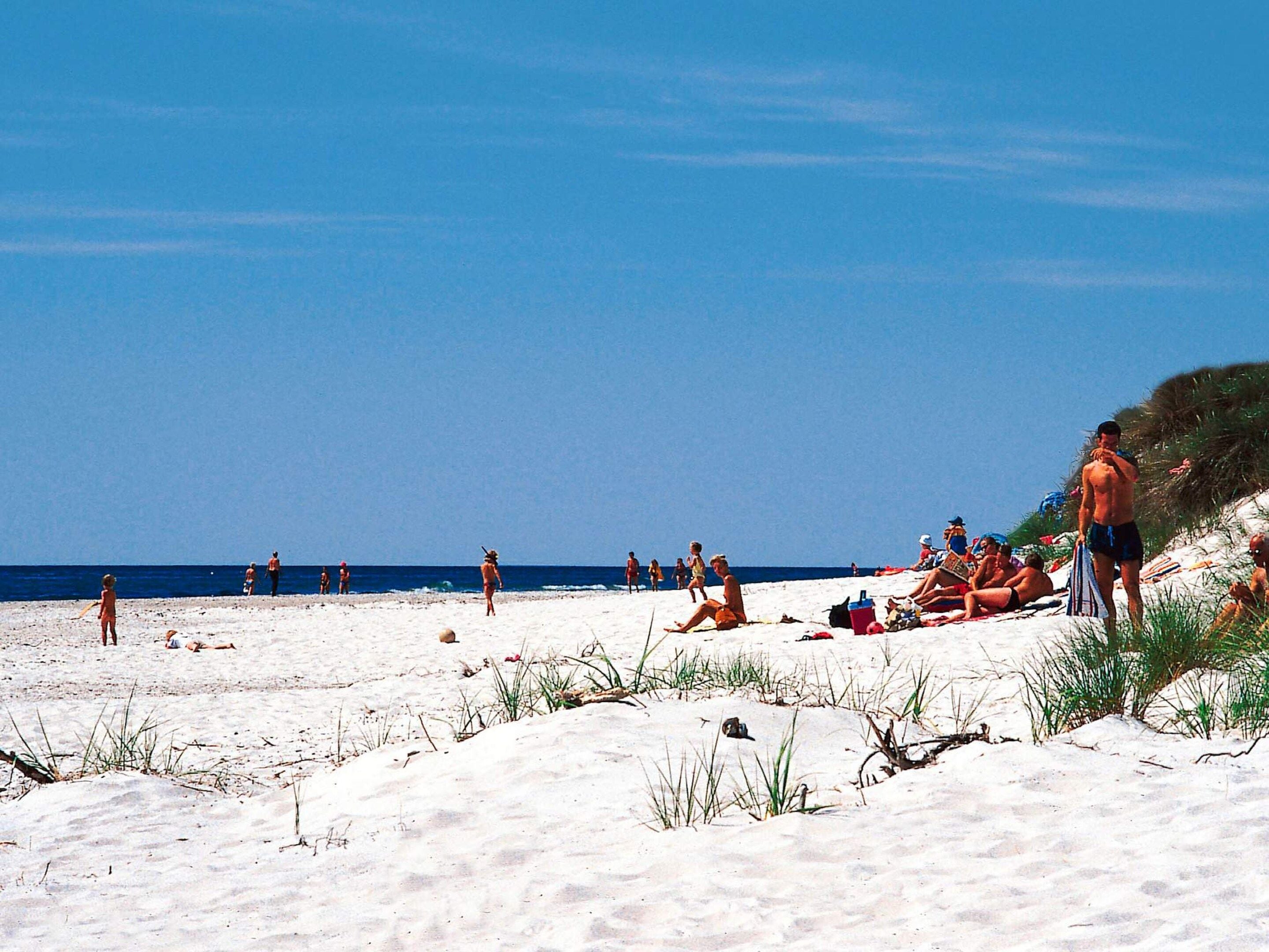 A beach with people sunbathing and walking, and a clear blue sky.
