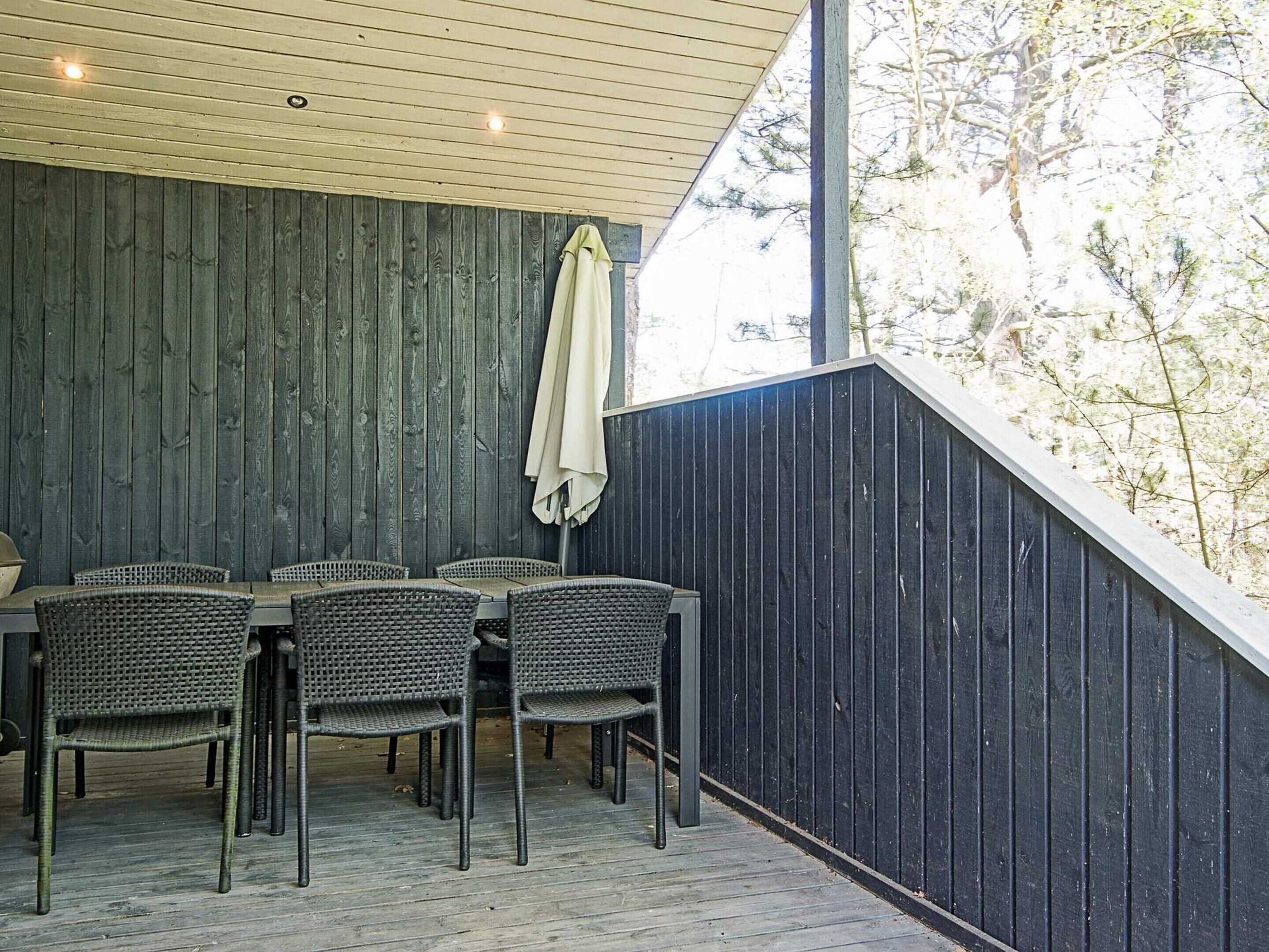 Un área de comedor al aire libre con una mesa y sillas, un muro de madera y vistas a árboles.