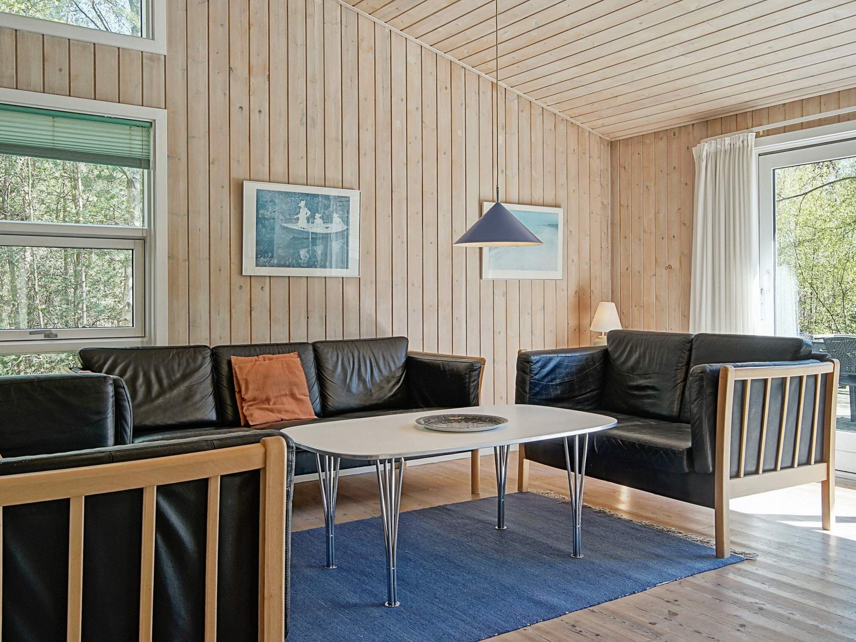A modern living room with a wooden paneled wall, a black leather sofa, a small table, and a lamp.
